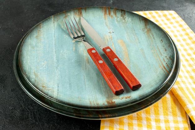 Bottom view dinner knife and a fork on plate on yellow and white checkered napkin on black ground