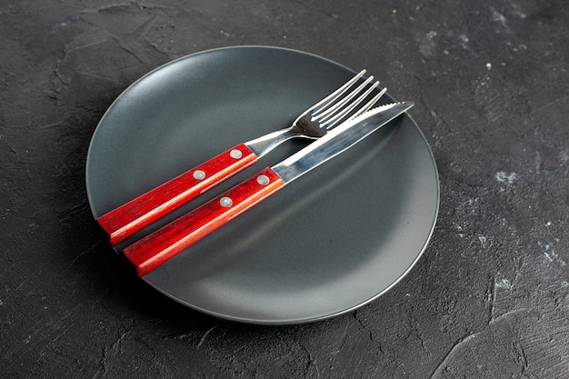 Free photo bottom view a fork and knife on black round platter on dark surface