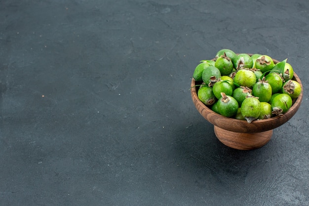 Bottom view fresh feijoas in wooden bowl on dark surface with copy space