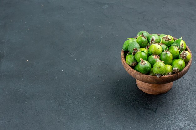 Bottom view fresh feijoas in wooden bowl on dark surface with copy space