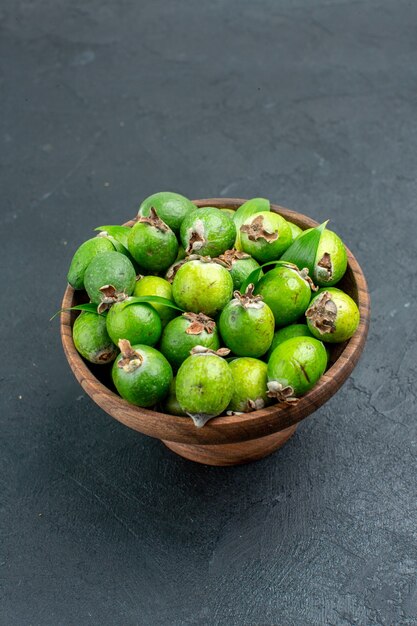 Bottom view fresh feijoas in wooden bowl on dark surface