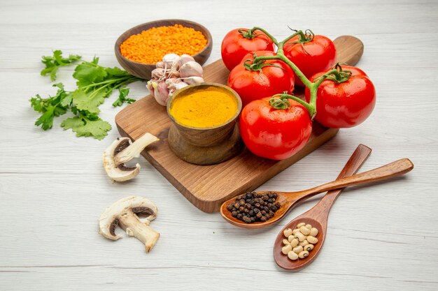 Bottom view fresh tomato branch garlic turmeric on chopping board mushrooms black pepper and beans in wooden spoons on grey table