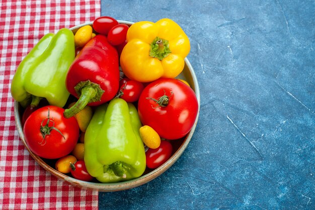 Free photo bottom view fresh vegetables cherry tomatoes different colors bell peppers tomatoes cumcuat on platter on red and white checkered tablecloth on blue table free space stock photo