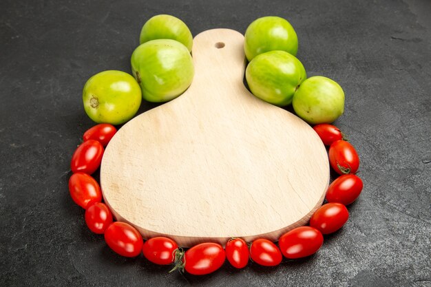 Bottom view green and red tomatoes around a chopping board on dark background