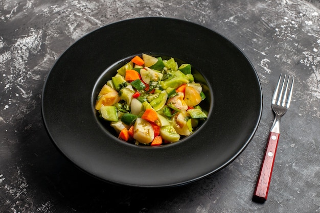 Bottom view green tomato salad on oval plate a fork on dark