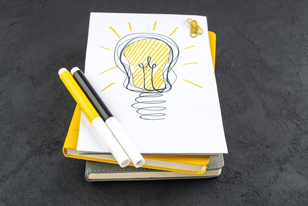 Bottom view ideaslight bulb on notepad yellow and black markers gem clips on black background