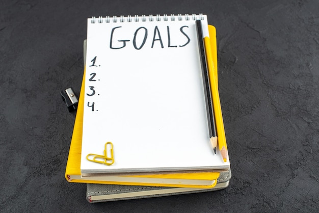 Bottom view list of goals written on notepad pencil sharpener black and yellow pencils gems clips on dark background