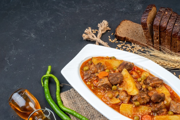 Free photo bottom view meat soup with garniture black bread green hot peppers oil bottle on table free space