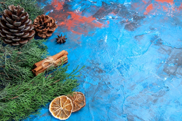 Bottom view pine tree branches with cones cinnamon sticks anise seed dried lemon slices on blue-red background with free place