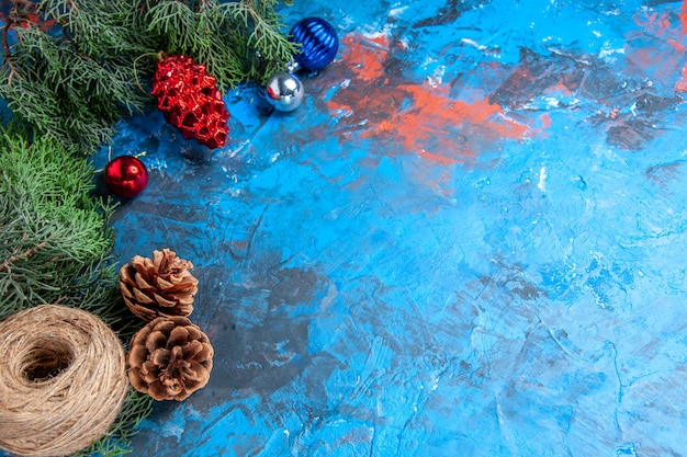 Bottom view pine tree branches with pinecones and colorful xmas tree toys straw thread on blue-red with free space