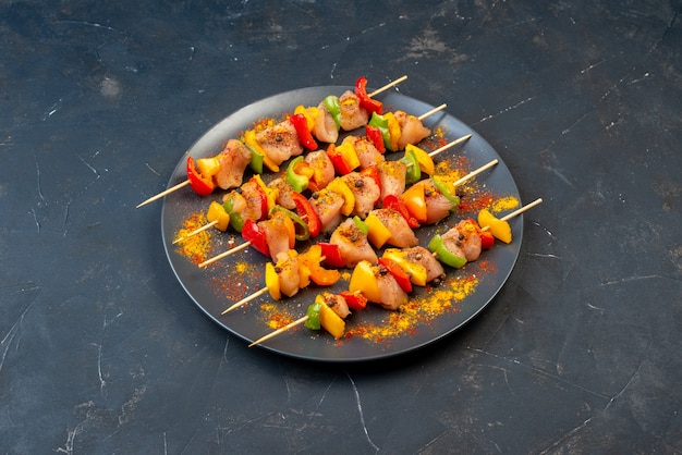 Bottom view raw chicken skewers with spices on wooden board on dark table free space