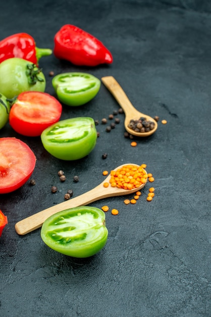 Free photo bottom view red and green tomatoes cut bell peppers black pepper cozy red lentils in wooden spoons on dark table