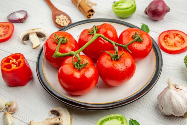 Bottom view red tomatoes on white plate garlic mushroom anises black-eyed peas in wooden spoon cinnamon sticks onion on grey table