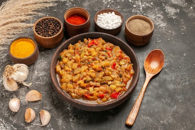 Free photo bottom view roasted eggplant salad in bowl different spices in bowls wooden spoon garlic on dark table