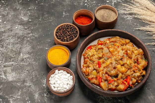 Bottom view roasted eggplant salad in bowl different spices in small bowls on dark table