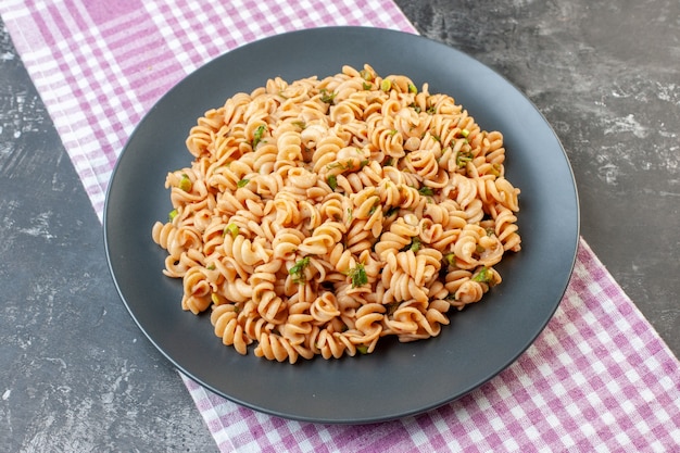 Bottom view rotini pasta on round plate on pink white checkered tablecloth on dark surface