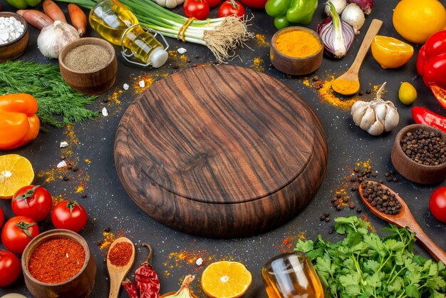 Bottom view round wooden board spices in small bowls tomatoes garlic coriander dill lemon on table