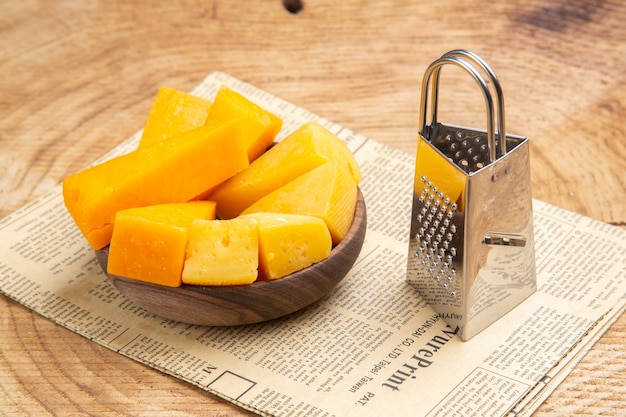 Free photo bottom view slices of cheese in bowl box grater on newspaper on wooden table