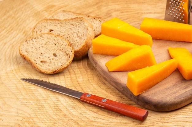 Bottom view slices of cheese box grater on cutting board knife bread slices on ground