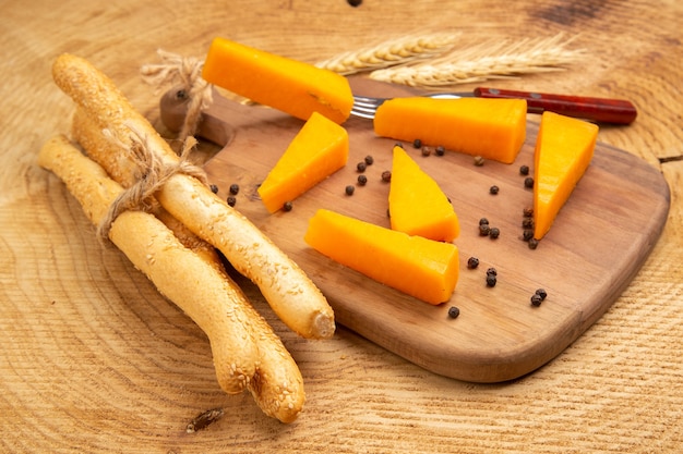 Bottom view slices of cheese scattered black pepper and fork on cutting board wheat spike bread on wooden table