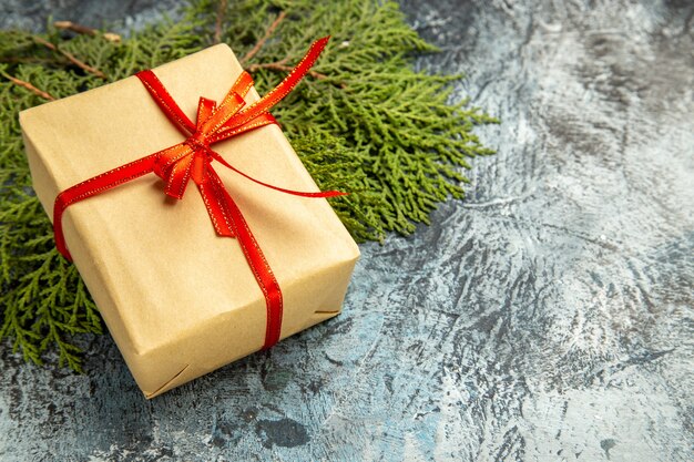 Free photo bottom view small gift tied with red ribbon on pine branches on dark