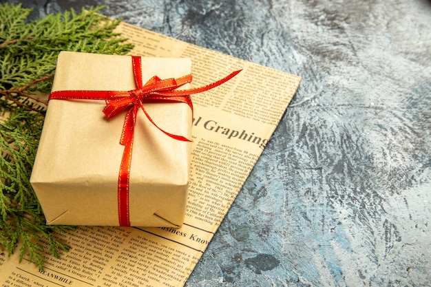 Bottom view small gift tied with red ribbon pine branches on newspaper on dark background copy space