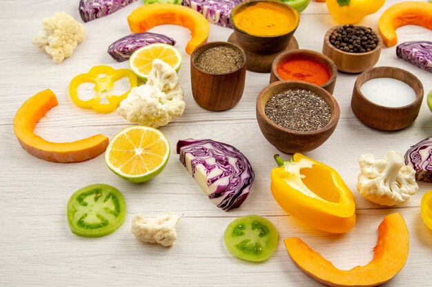 Bottom view spices bowls cut bell pepper cauliflower cut pumpkin cut red cabbage cut green tomatoes on white table