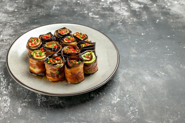 Bottom view stuffed aubergine rolls on white oval plate on grey