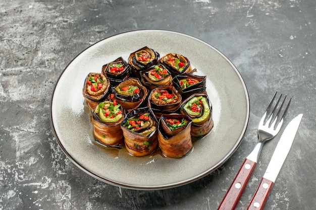 Bottom view stuffed eggplant rolls on white oval plate fork and knife on grey background