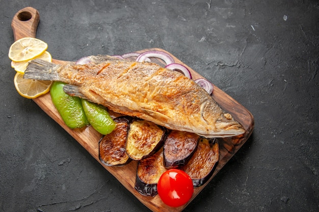 Bottom view tasty fish fry fried eggplants onion on wood serving board on dark background