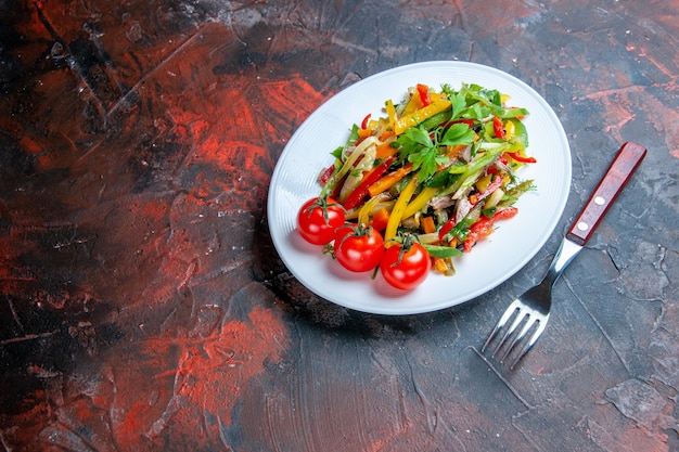 Bottom view vegetable salad on oval plate fork on dark surface free place