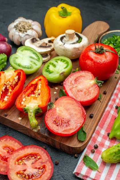 Free photo bottom view vegetables green and red tomatoes yellow bell pepper on cutting board greens in bowl knife cucumbers on red tablecloth on black table