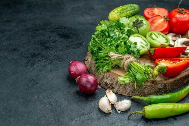 Bottom view vegetables mushrooms red and green tomatoes bell peppers greens on rustic board red onions hot peppers garlic on black table free space