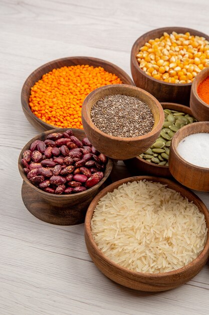 Bottom view wooden bowls with beans rice black pepper pumpkin seeds turmeric salt lentiles on grey table