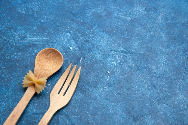 Bottom view wooden fork spoon farfalle on spoon on blue table free space