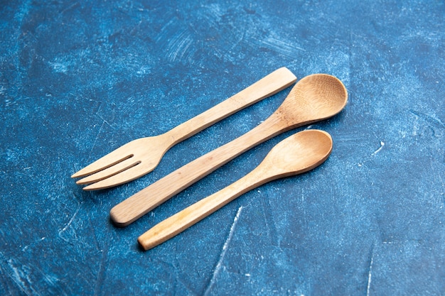 Free photo bottom view wooden fork spoon knife on blue surface free space