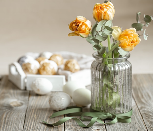 A bouquet of flowers in a glass vase with decorative elements on a blurred background. Easter holiday concept.