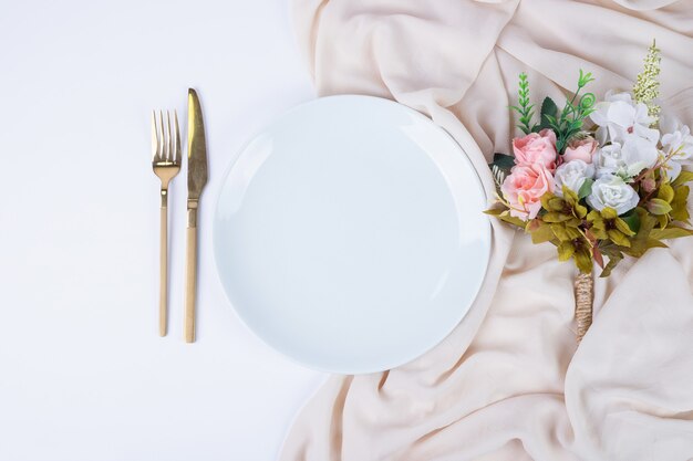 Bouquet of flowers, plate and cutlery on white surface.