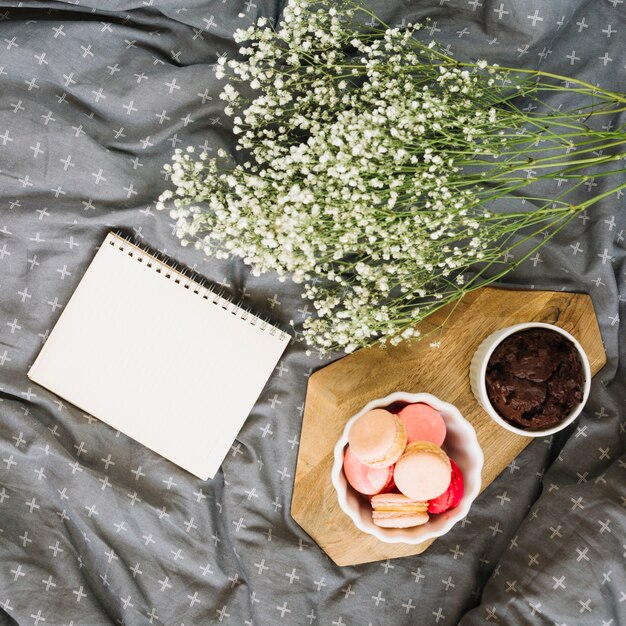 Bouquet near notepad and desserts on bed