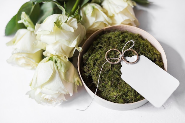 Free photo bouquet of roses and bowl of moss and wedding rings with blank tag