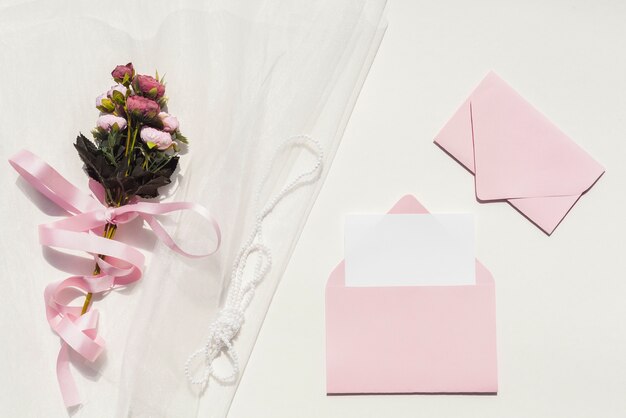 Bouquet of roses on veil next to wedding invitations