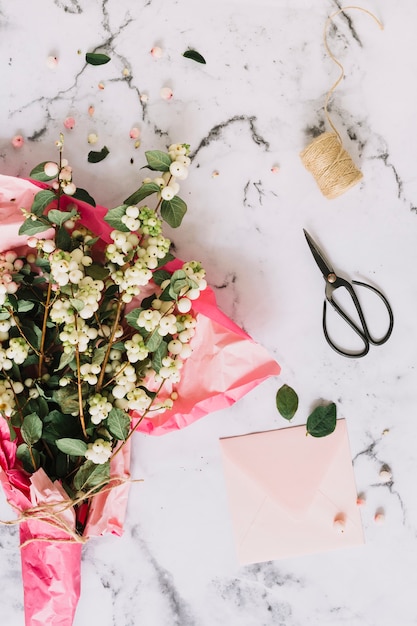 Free photo bouquet of symphoricarpos albus; common snowberry twigs wrapped in pink paper with scissor; spool and envelope