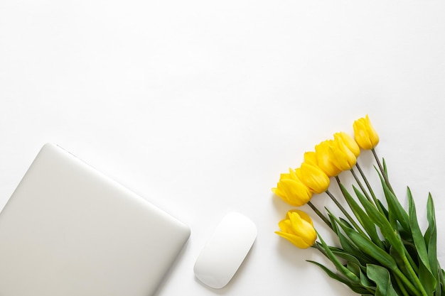 Free photo a bouquet of yellow tulips laptop and a computer mouse on a white background