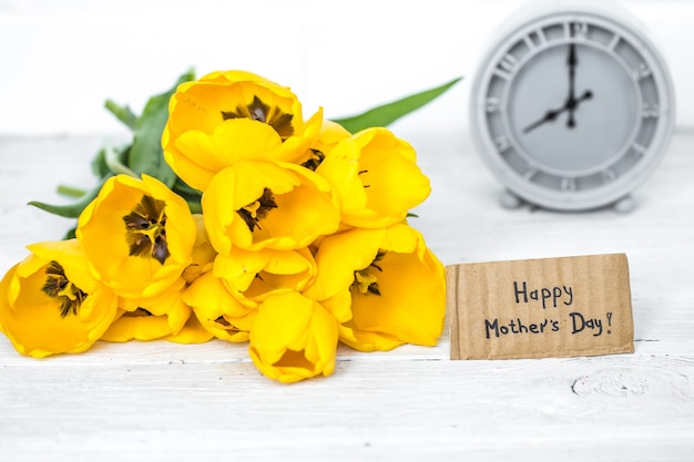 bouquet of yellow tulips and a retro clock on a bright wooden background,space for text,concept of the holiday