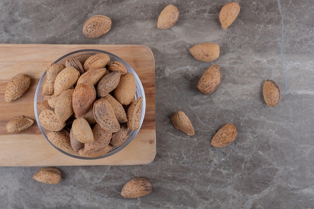 Free photo a bowl of almonds on a tray and scattered almonds on the marble surface