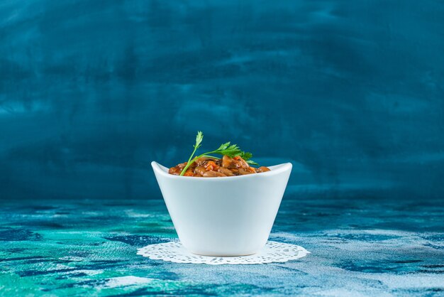 A bowl of baked beans on a coaster, on the blue background. 