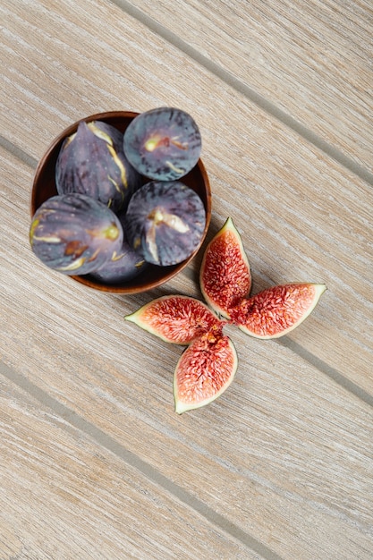 Free photo a bowl of black figs and slices of figs on a wooden table