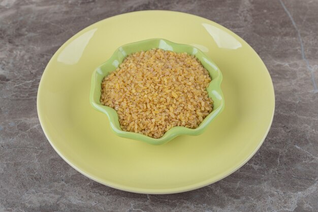 A bowl of bulgur on the plate on the marble surface