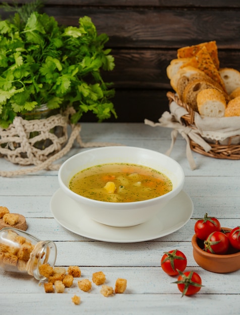 Free photo a bowl of chicken soup with potato, carrot and dill served with bread slices