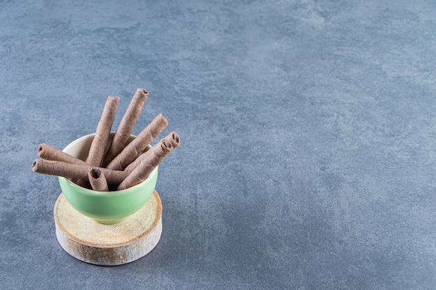 Free Photo a bowl of chocolate wafer rolls on a board , on the marble background.